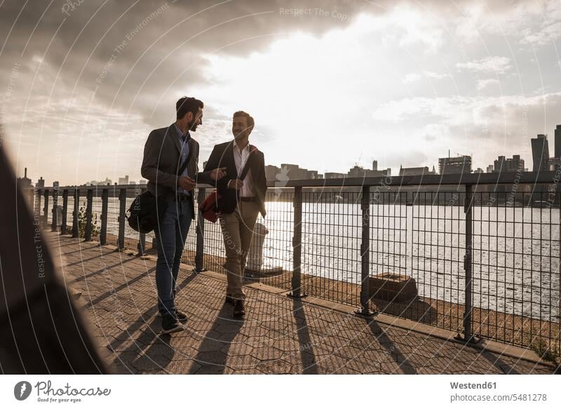 USA, New York City, two businessmen walking along East River man males smiling smile going Businessman Business man Businessmen Business men New York State