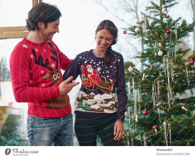 Couple standing in front of Christmas tree wearing Christmas jumpers caucasian caucasian ethnicity caucasian appearance european knit pullover knit sweater