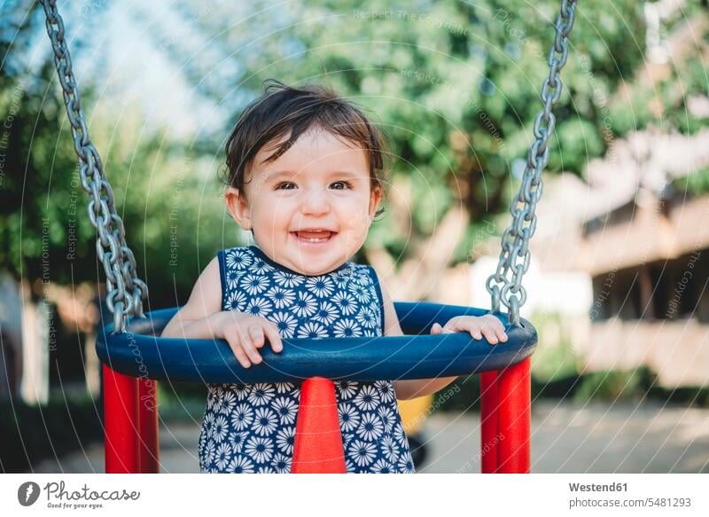 Portrait of laughing baby girl sitting in swing on playground swing set swingset baby girls female portrait portraits babies infants people persons human being