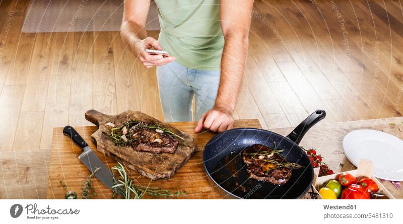 Man with prepared steaks in kitchen using celll phone caucasian caucasian ethnicity caucasian appearance european Germany indoors indoor shot Interiors