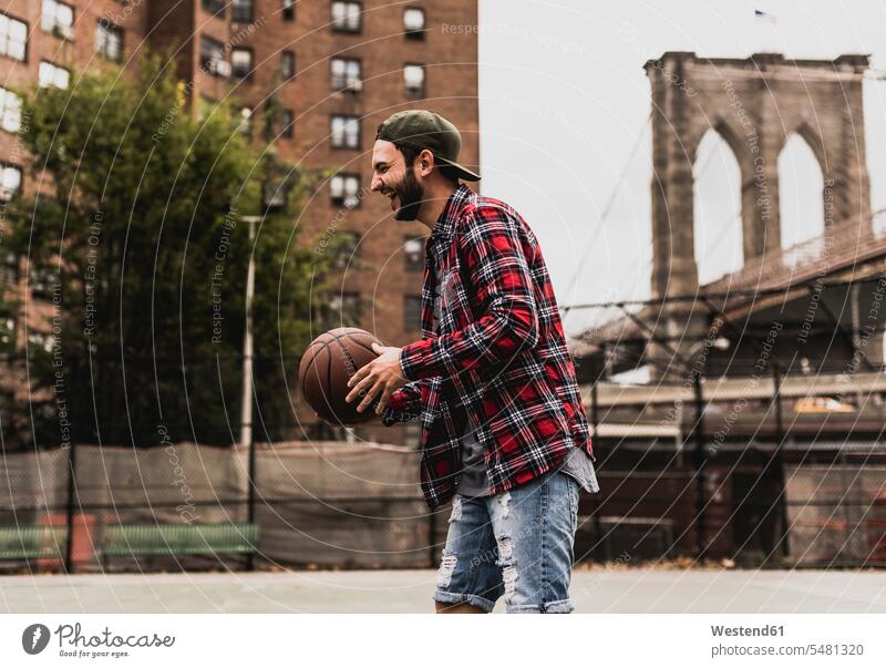 USA, New York, laughing young man with basketball on an outdoor court exercising exercise training practising playing basketballs Laughter men males Basketball