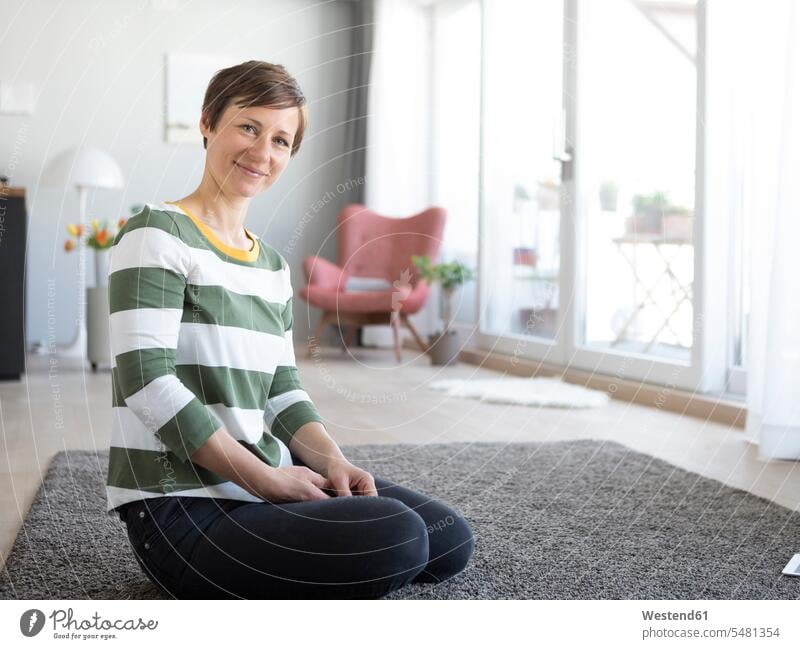 Portrait of smiling woman sitting on the floor in the living room portrait portraits living rooms livingroom females women domestic room domestic rooms Adults