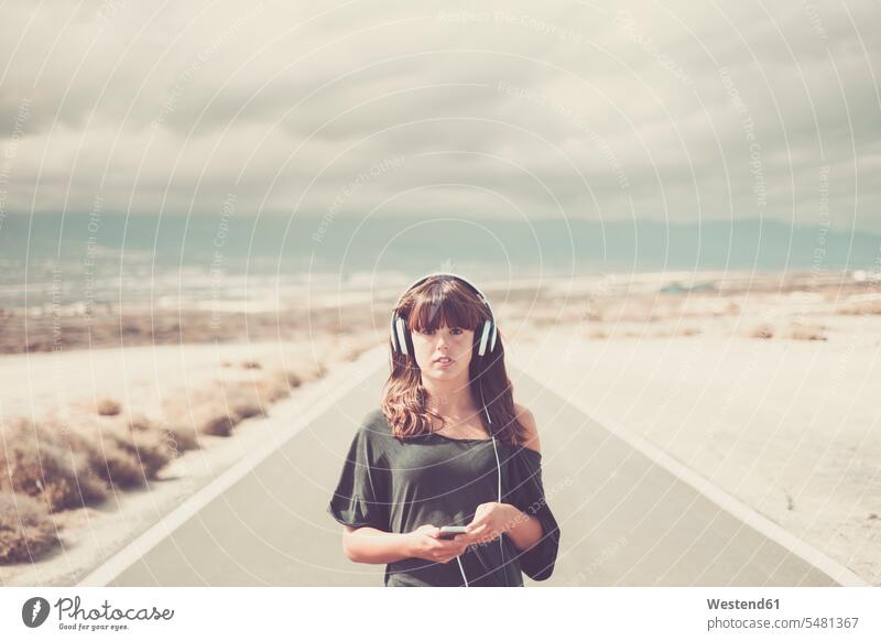 Young woman on the road listening music with headphones headset hearing streets roads females women Smartphone iPhone Smartphones journey travelling Journeys