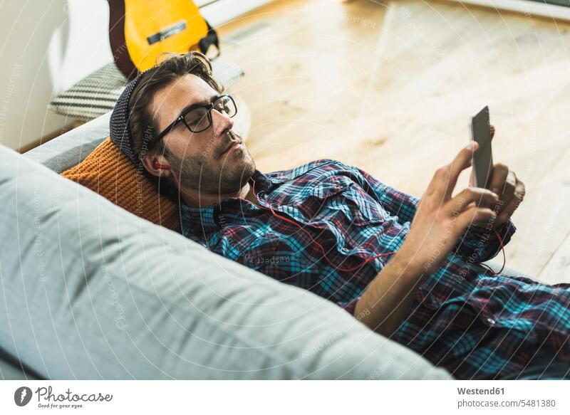 Young man lying on the couch hearing music with earphones and smartphone shirt shirts leaning rested on lying on back laying on back dorsal position MP3 Player