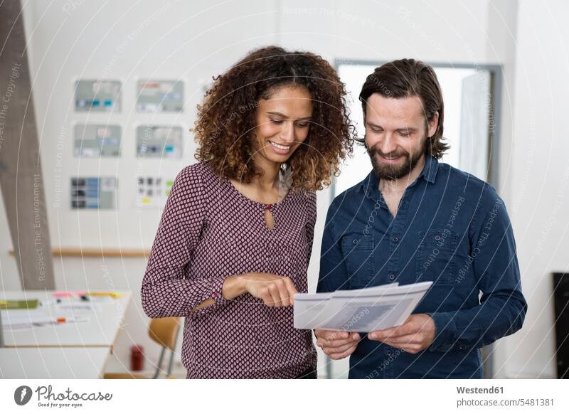 Two colleagues discussing papers in office working At Work offices office room office rooms workplace work place place of work smiling smile tablet digitizer