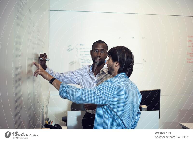 Business people writing on whiteboard in office presentation presentations discussing discussion Whiteboard pointing point at pointing at show showing write