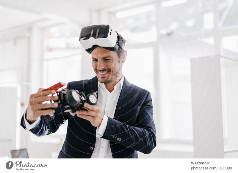 Smiling businessman wearing VR glasses looking at toy racing car 3D Glasses 3-D Glasses men males Businessman Business man Businessmen Business men
