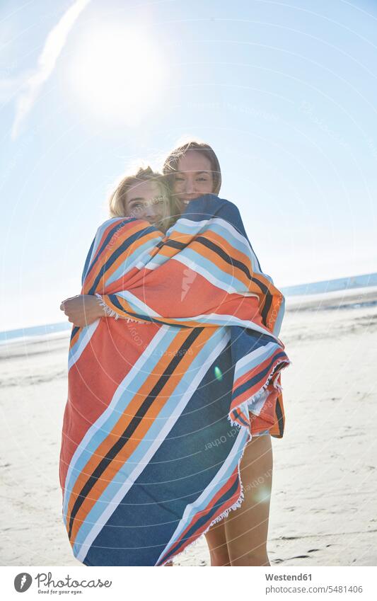 Two young women wrapped in a blanket on the beach woman females female friends Blanket Blankets smiling smile vacation Holidays beaches Adults grown-ups