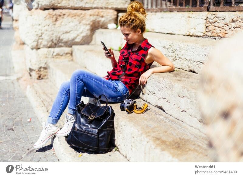 Italy, Verona, woman sitting on stairs looking at cell phone mobile phone mobiles mobile phones Cellphone cell phones smiling smile females women telephones