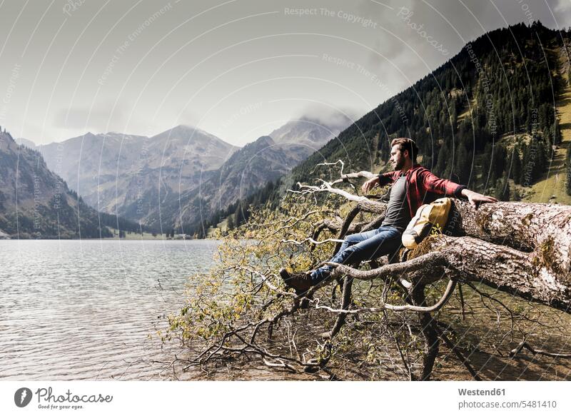 Austria, Tyrol, Alps, hiker relaxing on tree trunk at mountain lake Tree Trunk Tree Trunks lakes wanderers hikers man men males sitting Seated Trees water