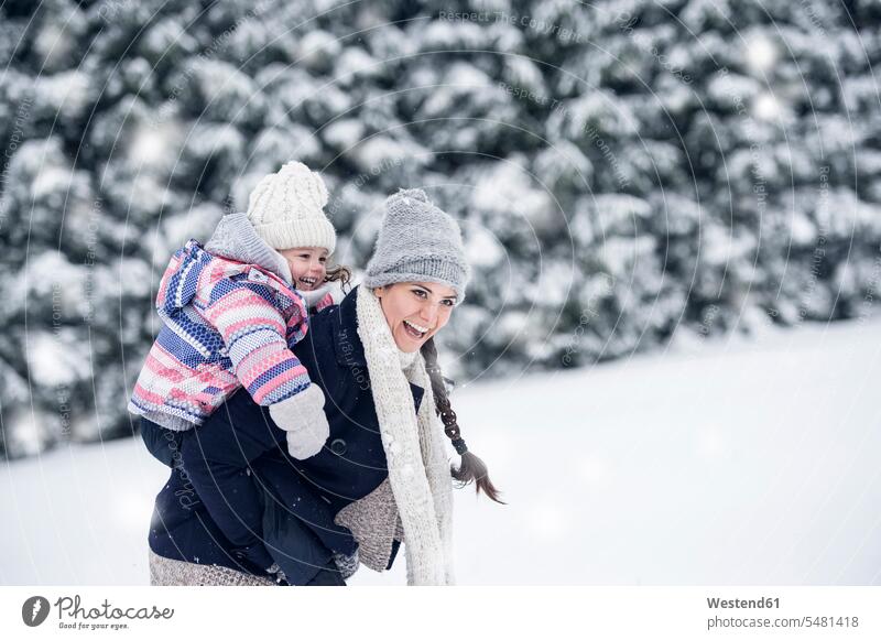 Happy mother carrying daughter piggyback in winter landscape daughters hibernal laughing Laughter mommy mothers ma mummy mama child children family families