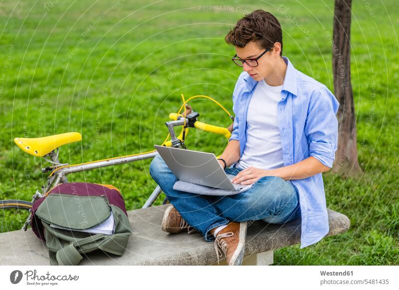 Young man with racing cycle sitting on a bench using laptop Laptop Computers laptops notebook men males computer computers Adults grown-ups grownups adult