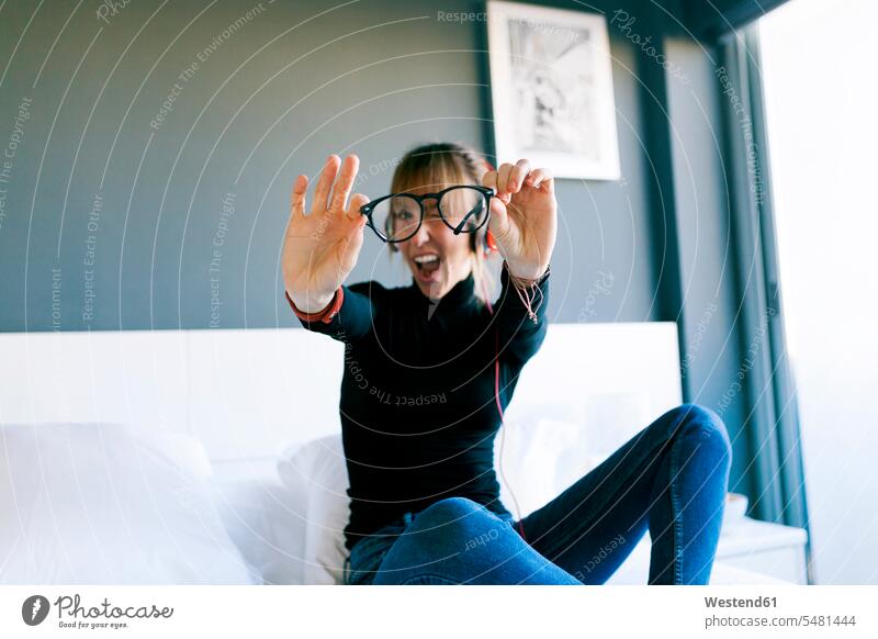 Young woman on bed holding her glasses specs Eye Glasses spectacles Eyeglasses females women beds Adults grown-ups grownups adult people persons human being
