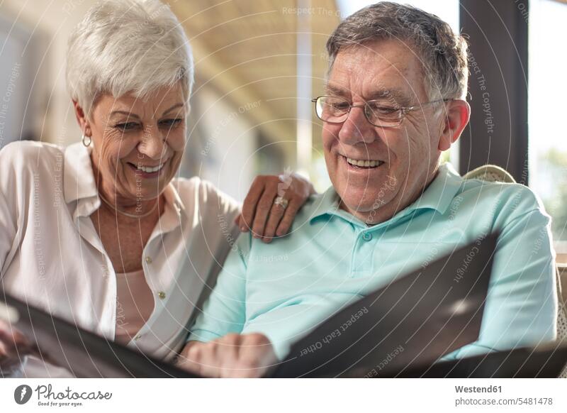Happy senior couple sitting on couch looking at photo album settee sofa sofas couches settees eyeing happiness happy home at home twosomes partnership couples