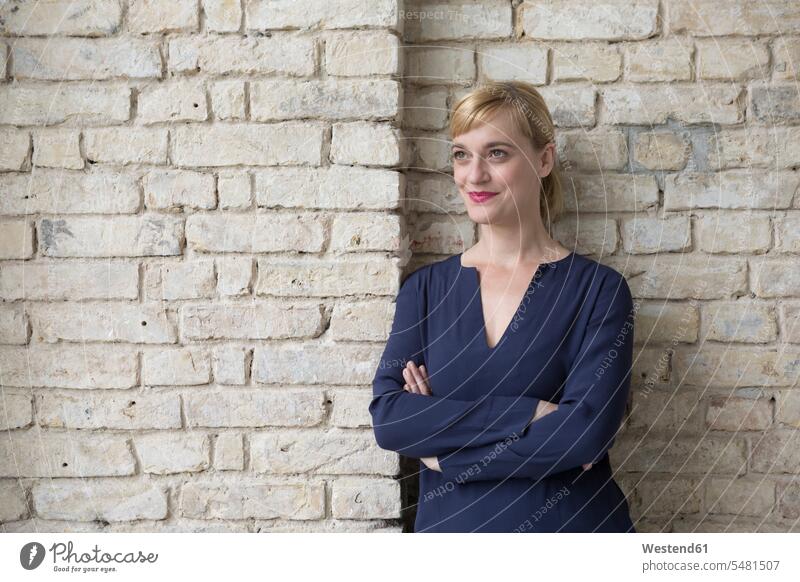 Businesswoman leaning against brick wall, looking away confidence confident smiling smile brick walls standing daydreaming day dreaming Daydreams Day Dream