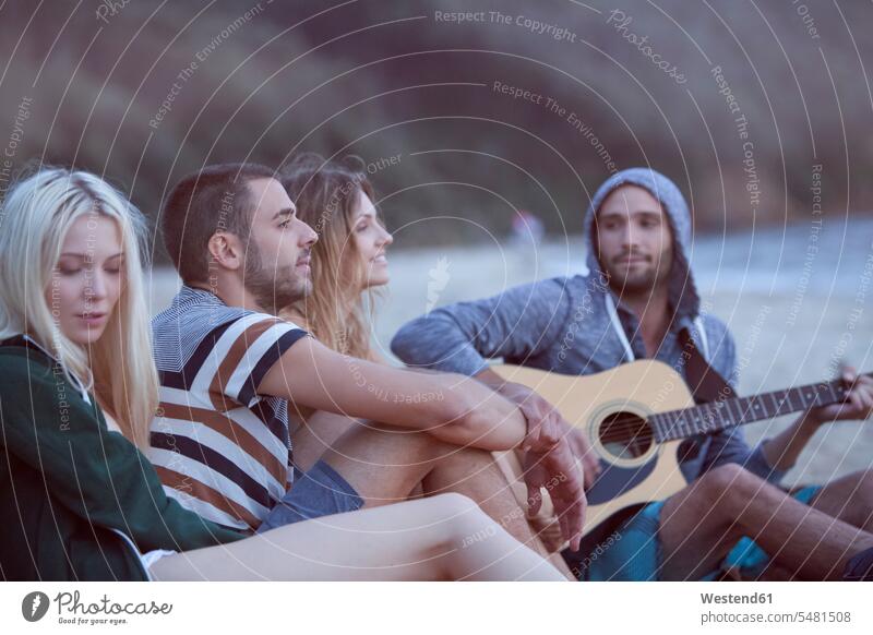Four friends at the beach making music Fun having fun funny happiness happy friendship community Companionship sitting Seated Quality Time playing music