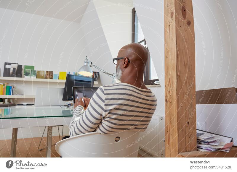 Back view of man sitting at desk of his home office using smartphone African-American Ethnicity Afro-American African American Ethnicity African Americans