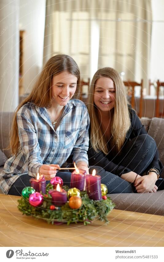 Young woman lighting candle on Advent wreath while her friend is watching Upper Bavaria togetherness confidence confident traditional culture growing up