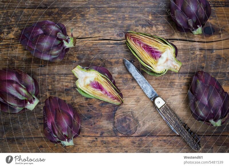 Sliced and whole purple organic artichokes and a pocket knife on dark wood uncooked wooden pocket knives overhead view from above top view Overhead