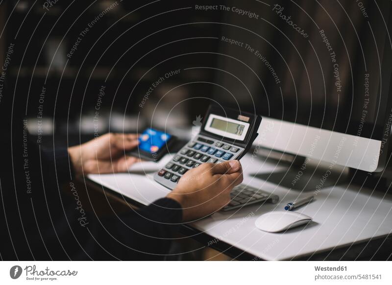 Man using calculator and credit card at desk, partial view hand human hand hands human hands debit card people persons human being humans human beings cashless