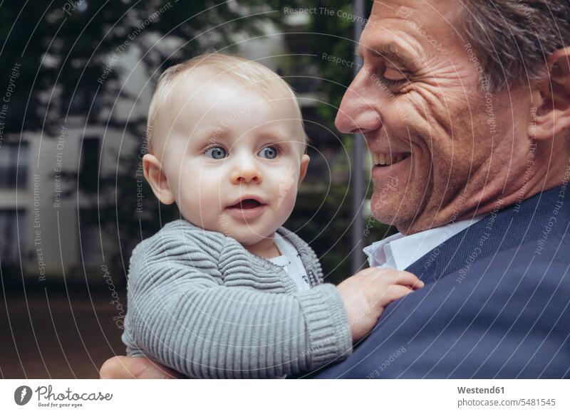 Happy mature businessman holding baby boy outdoors Businessman Business man Businessmen Business men father pa fathers daddy dads papa infants nurselings babies