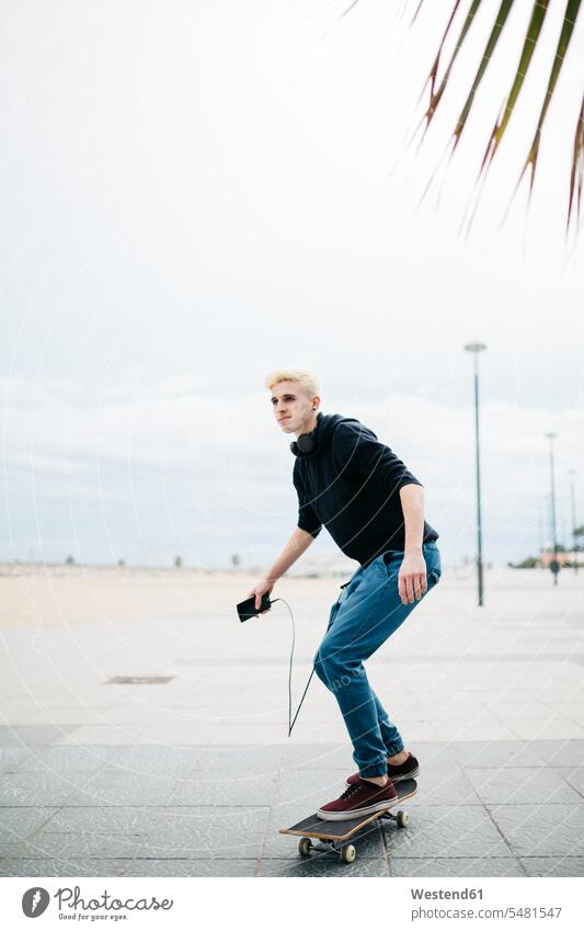 Spain, Torredembarra, young man with smartphone standing on his skateboard caucasian caucasian ethnicity caucasian appearance european on the move on the way