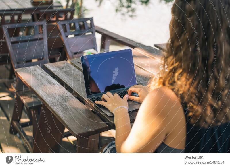 Young woman sitting outdoors, using laptop Table Tables working At Work Seated writing write vacation Holidays young women young woman Travel females Adults