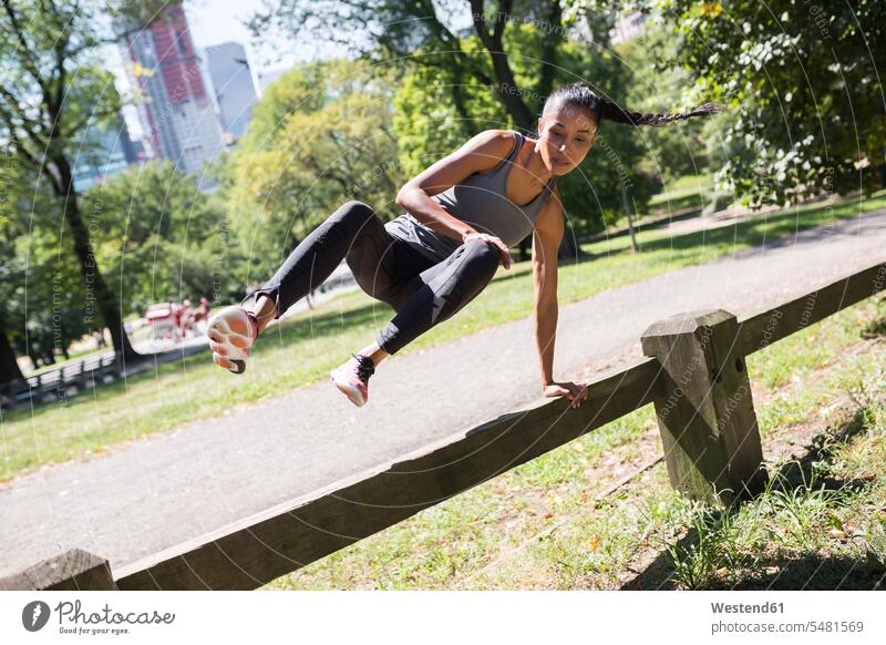 Woman jumping over fence in park woman females women exercising exercise training practising Leaping Adults grown-ups grownups adult people persons human being