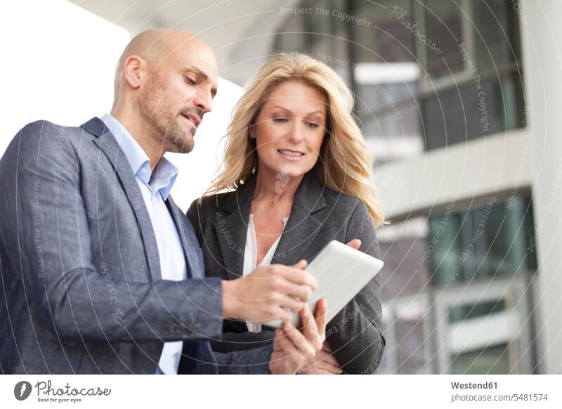 Businessman and businesswoman with digital tablet outdoors businesswear business attire business clothing communication talking conversations smiling smile