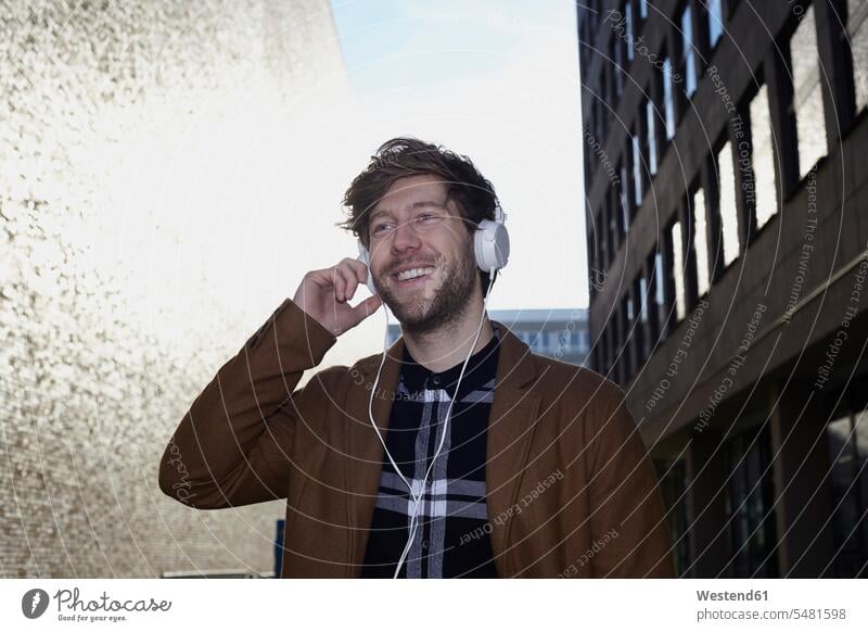 Smiling young man listening music with headphones at backlight caucasian caucasian ethnicity caucasian appearance european brown hair brown haired brown-haired