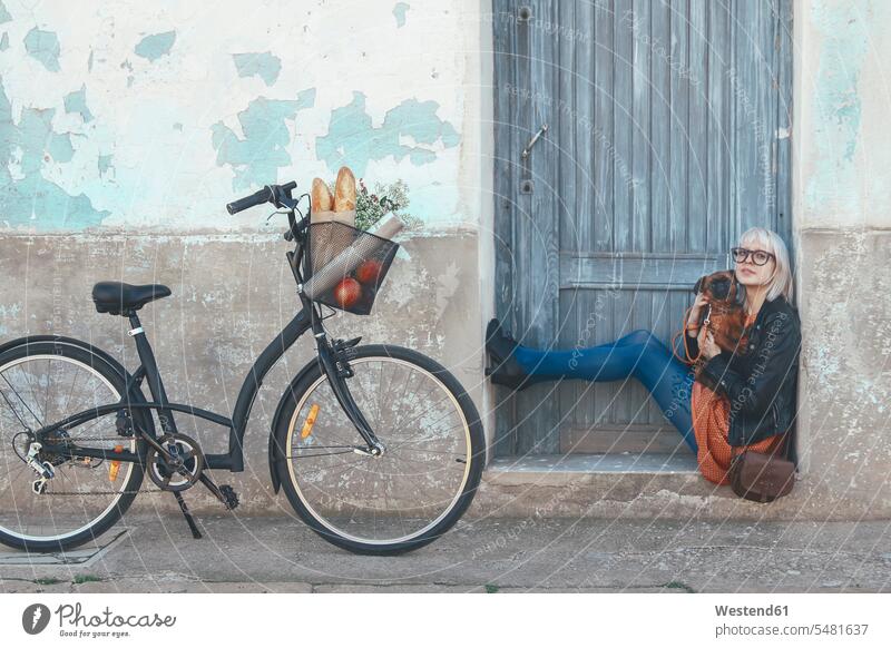 Young woman sitting in door frame holding dog dogs Canine bicycle bikes bicycles females women pets animal creatures animals Adults grown-ups grownups adult