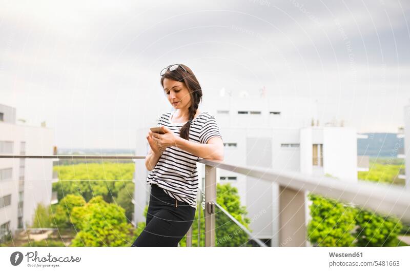 Woman using smartphone on balcony woman females women balconies roof terrace deck rooftop Adults grown-ups grownups adult people persons human being humans