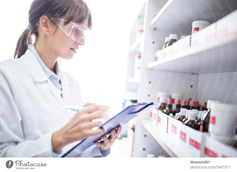Woman holding clipboard in laboratory of a pharmacy Apothecary drugstores pharmacies clipboards clip-board clip-boards clip board woman females women workplace