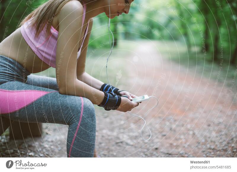Sporty woman having a break in forest woods forests sportive sporting sporty athletic exercising exercise training practising mobile phone mobiles mobile phones
