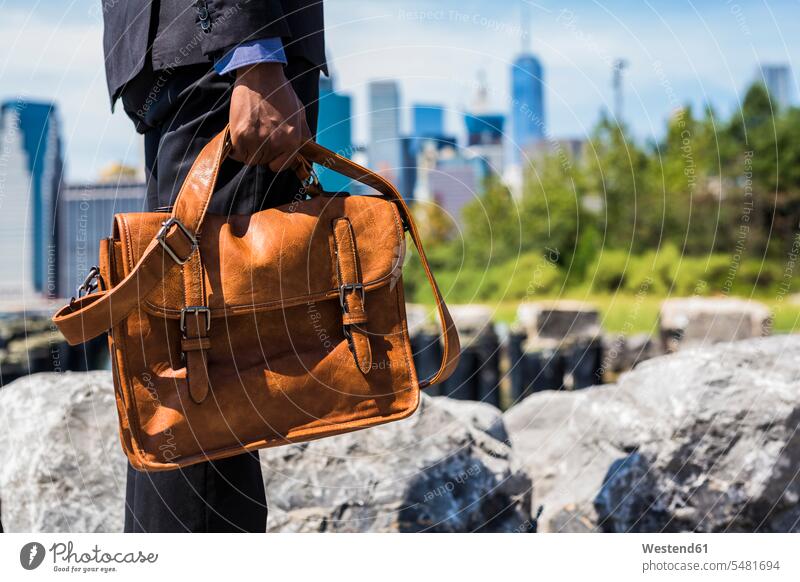 USA, Brooklyn, businessman with briefcase standing in front of Manhattan skyline, partial view Businessman Business man Businessmen Business men bag bags