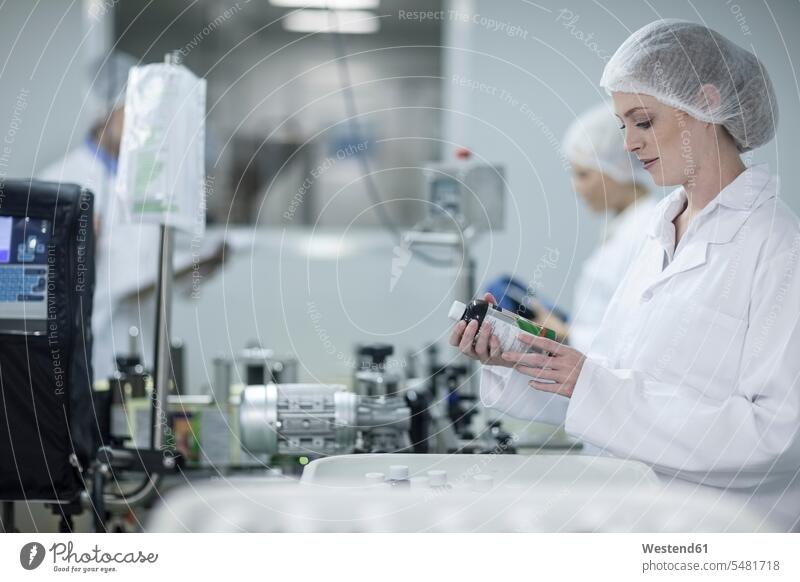 Woman in pharmaceutical plant looking at flask working At Work factory factories Flasks woman females women Adults grown-ups grownups adult people persons
