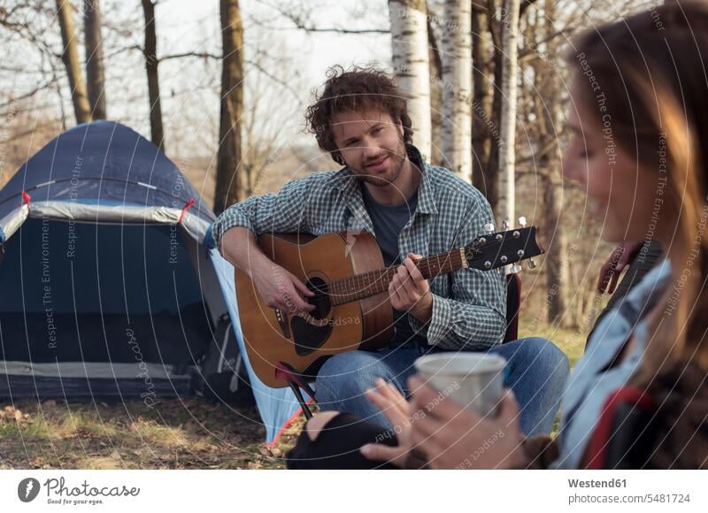 Couple camping in forest with man playing guitar smiling smile woods forests couple twosomes partnership couples guitars people persons human being humans