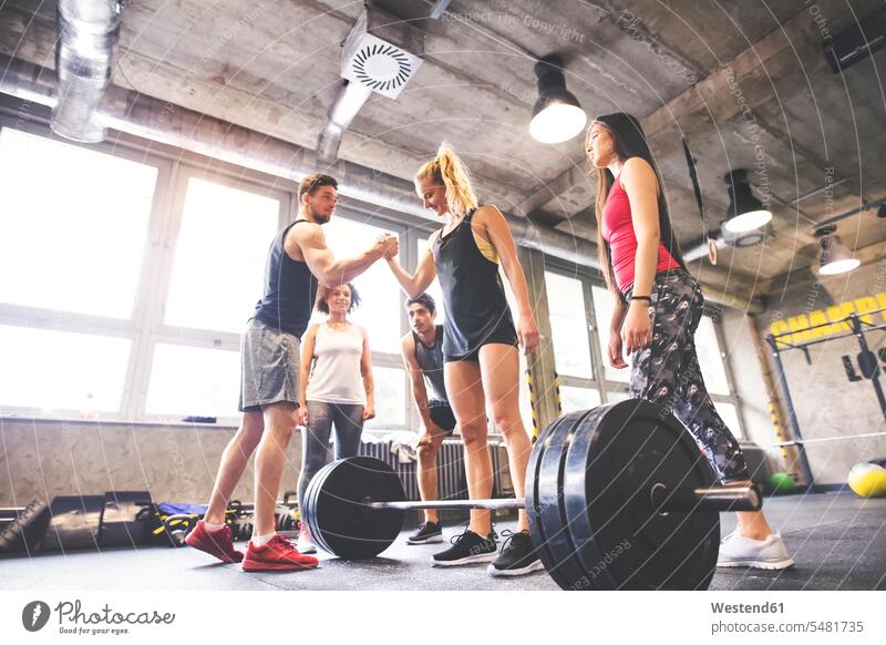 Group of young fit people motivating woman weightlifting in gym weight lifting exercising exercise training practising strength sports fitness Fitness training
