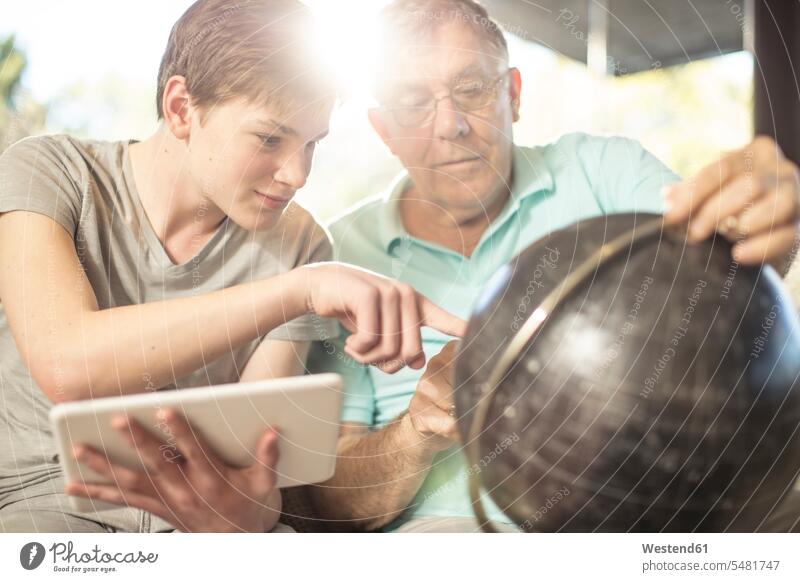 Gandfather and grandson together looking at earth globe home at home globes grandsons eyeing grandfather grandpas granddads grandfathers senior men senior man