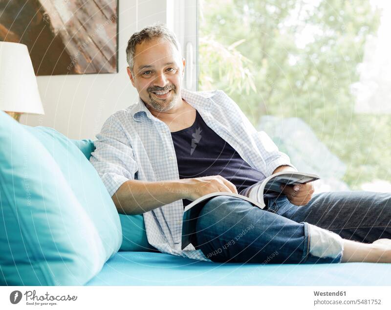 Portrait of smiling man sitting on the couch with magazine men males settee sofa sofas couches settees Adults grown-ups grownups adult people persons