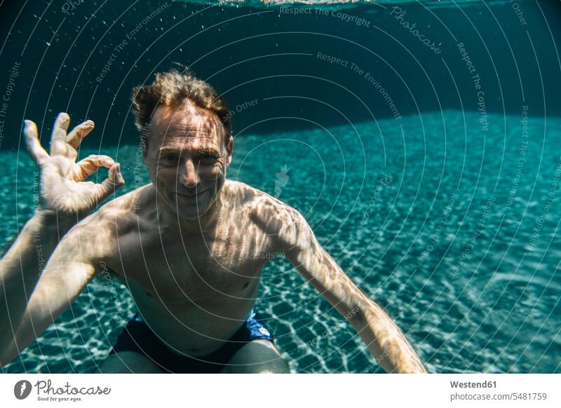 Portrait of smiling man underwater in a swimming pool making ok sign smile pools swimming pools men males portrait portraits submerged Under Water