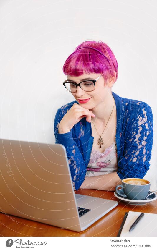 Portrait of smiling young woman with dyed hair sitting in a coffee shop looking at laptop Laptop Computers laptops notebook smile females women computer