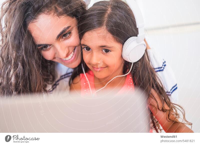 Happy teenage girl and her little sister with laptop and headphones females girls headset sisters smiling smile happiness happy child children kid kids people