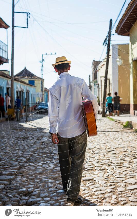 Cuba, Trinidad, back view of man with guitar walking on the street men male adults males street musician street musicians Adults grown-ups grownups people