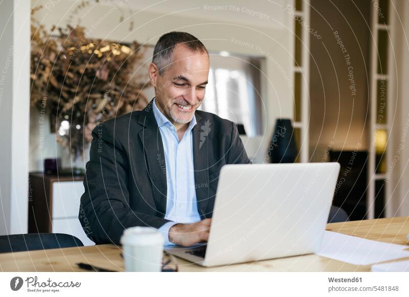 Successful businessman sitting at desk, working om laptop successful Seated At Work Laptop Computers laptops notebook desks Office Offices Businessman