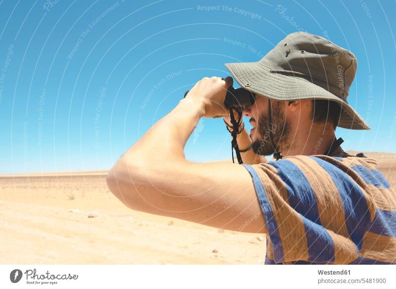 Namibia, Namib desert, man with hat using binoculars to look away caucasian caucasian ethnicity caucasian appearance european nature tourism cap caps casual