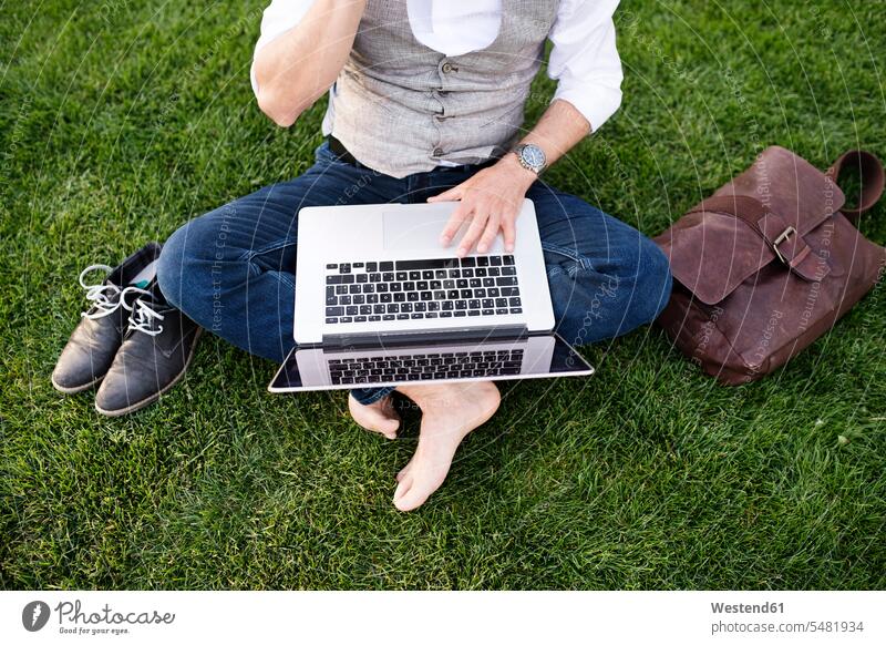 Unrecognizable businessman with laptop sitting on grass Laptop Computers laptops notebook Businessman Business man Businessmen Business men meadow meadows