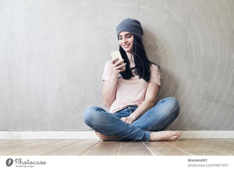 Smiling young woman sitting on the floor using cell phone mobile phone mobiles mobile phones Cellphone cell phones smiling smile females women Seated telephones