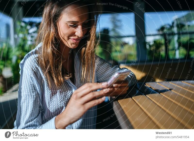 Smiling woman on terrace looking at cell phone females women terraces Smartphone iPhone Smartphones Adults grown-ups grownups adult people persons human being