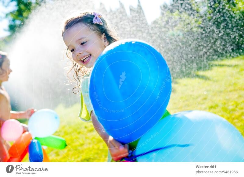 Little girl with balloons having fun with lawn sprinkler in the garden females girls child children kid kids people persons human being humans human beings